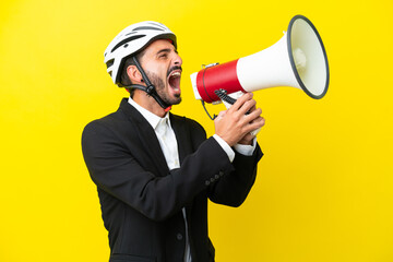 Fototapeta premium Business caucasian man with a bike helmet isolated on yellow background shouting through a megaphone