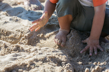 Toddler playing on a beach with fine sand, one person, touching