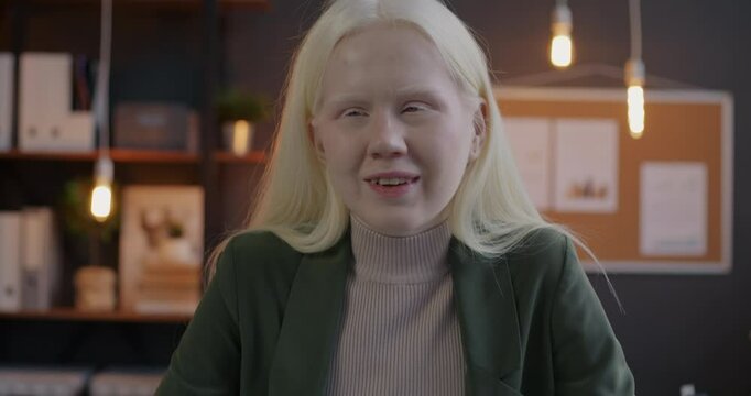 Portrait of beautiful albino woman office worker making online video call speaking looking at camera in inclusive workplace in evening. Job and communication concept.