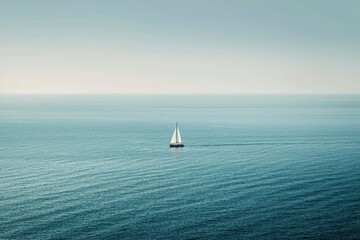Fototapeta premium A small boat sailing on a vast ocean, with the distant coastline blurred out. 