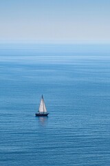 Fototapeta premium A small boat sailing on a vast ocean, with the distant coastline blurred out. 
