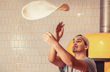 Skilled chef preparing dough for pizza rolling with hands and throwing up. Hands of a male chef...