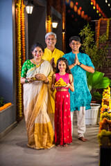 Fototapeta premium Indian parents with children celebrating Diwali on the balcony, holding Pooja thali and sweets.