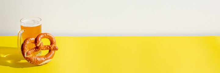 Glass of beer and pretzel on bright yellow table, celebrating Oktoberfest