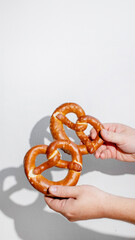 Two hands holding freshly baked pretzels on a white background, perfect for Oktoberfest celebrations and German cuisine concepts