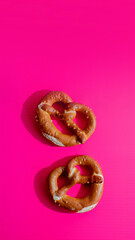 Two fresh pretzels on a bright pink background, perfect for celebrating Oktoberfest or illustrating snack cravings