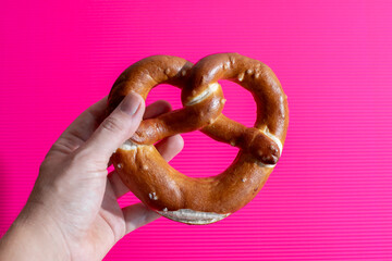 Hand holding a fresh pretzel on vibrant pink background, perfect for Oktoberfest or German-themed culinary concepts