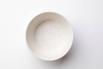 A white ceramic bowl filled with sea salt on a plain background, emphasizing simplicity and minimalism in cooking