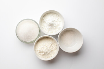 Top view of four bowls filled with white powder ingredients on a white background, symbolizing baking preparation for holidays