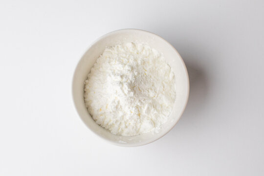 White powder in a bowl, zoomed in on a white background, commonly used for baking during Christmas holidays