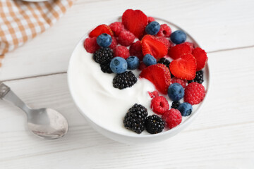 Bowl of tasty yogurt with different fresh berries on white wooden background
