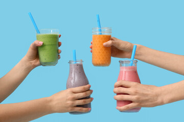 Female hands with glasses and bottles of different fresh smoothie on blue background