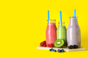 Bottles of fresh smoothie with different berries on yellow background