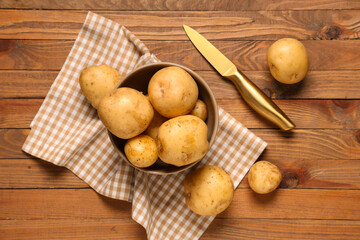 Bowl with raw potatoes and knife on wooden background