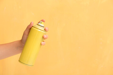 Female hand with spray paint can near yellow wall
