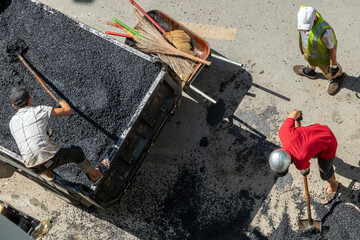 A workers loads crushed asphalt onto the bed of a truck