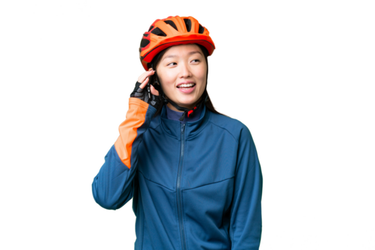 Young cyclist woman over isolated chroma key background keeping a conversation with the mobile phone