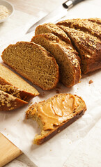 Homemade yeasted banana oatmeal bread with creamy peanut butter, over white background. Selective focus