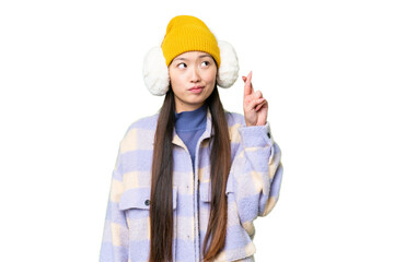 Young Asian woman wearing winter muffs over isolated chroma key background with fingers crossing and wishing the best