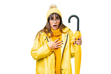 Young caucasian woman with rainproof coat and umbrella over isolated chroma key background surprised and shocked while looking right
