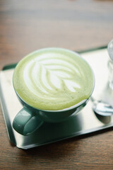 A close-up shot of a matcha latte with intricate latte art, served in a green cup on a wooden table, perfect for coffee and tea enthusiasts.