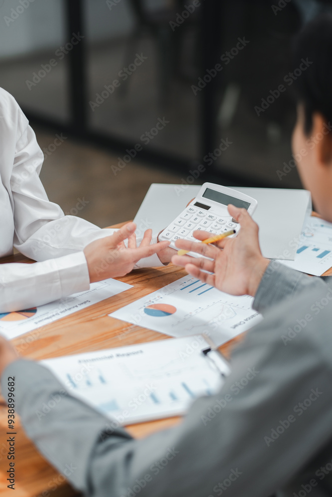 Poster colleagues discussing financial reports and using a calculator during a business meeting in a modern