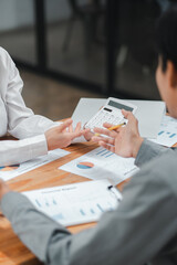 Colleagues discussing financial reports and using a calculator during a business meeting in a modern office setting.