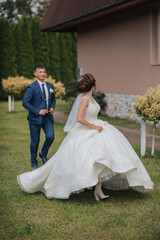 A bride and groom are walking down a grassy path. The bride is wearing a white dress and the groom is wearing a blue suit