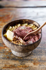 A healthy smoothie Acai bowl with fruits banana apple with spoon on a wooden table