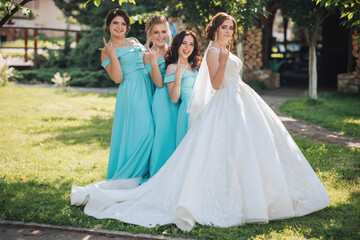 A bride and her bridesmaids pose for a picture in a grassy field. The bride is wearing a white...