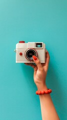 A striking hand holding a white vintage camera with red accents against a solid teal wall, showcasing a fusion of retro style and vibrant color.