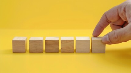 A person arranges six wooden blocks on a bright yellow background during a creative activity focused on building and design
