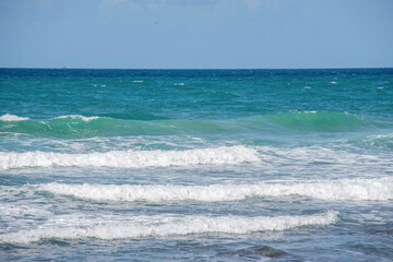 Fototapeta premium Waves Rolling Gently Onto Sunlit Shoreline With Clear Blue Water on Calm Day