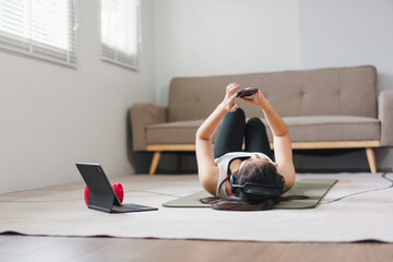 Young Asian woman at home doing exercise in front of open laptop, repeating instructions by professional online fitness trainer.