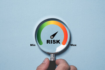 Hand holding magnifier glass with Risk level indicator rating since low to high on blue background...