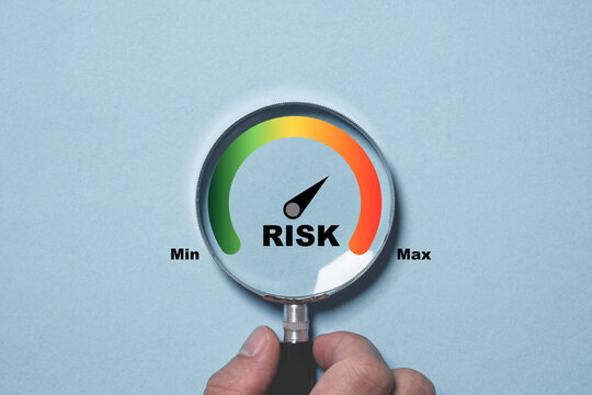 Hand holding magnifier glass with Risk level indicator rating since low to high on blue background for focus risk management and assessment concept.