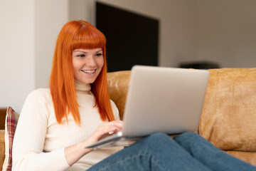 Young Woman With Orange Hair Uses  Laptop While Sitting on Couch at Home in Morning