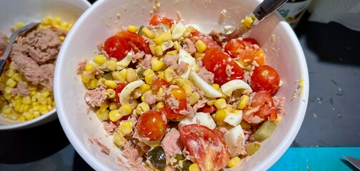 Close-up of a colorful and fresh mixed salad with tuna, corn, cherry tomatoes, boiled eggs, and pickles in a white bowl, showcasing a healthy and vibrant meal