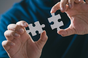 Close-up of hands holding two puzzle pieces, symbolizing connection, problem-solving, and...