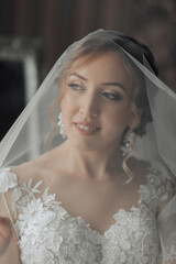 A bride is wearing a veil and smiling. The veil is white and has a lace design. The bride's dress...