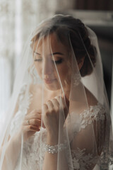 A woman is wearing a veil and is looking at the camera. The veil is made of lace and is covering...