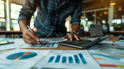Fototapeta premium A young male businessman in business clothes at his desk calculates a financial report, analysis using charts and graphs. Business concept.