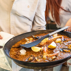 waiter holds typical Spanish paella. Made with rice, seafood, pepper, saffron, lemon, prawns, mussels and snails