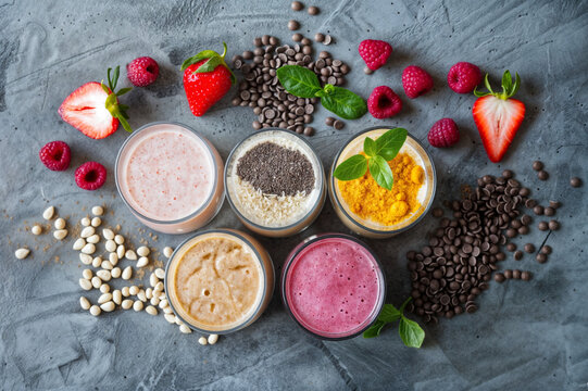 Cenital de batidos de frutas con frutas a su al rededor, fresas , frambuesas y semillas.