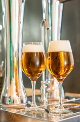 Two glasses of ice cold beer with foam are on the table in a bar next to the beer taps