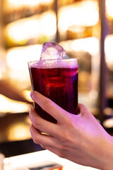 a hand holds a glass full of wine with lemon soda and ice, in a bar