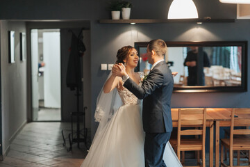 A bride and groom are dancing in a room with a lot of chairs. The chairs are arranged in a circle around the couple