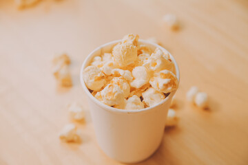 A bucket of popcorn, top-view, warm colors, light brown wooden background, flat lay, daylight macro close-up