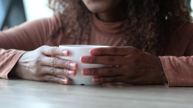 Women's hands hold a mug of hot tea in the morning during the cold season. A young woman warms her hands on a very hot cup of tea.