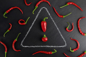 red hot chilies on a black slate plate with warning sign drawn with chalk, exclamation mark made from chilies, warning of spicy food concept